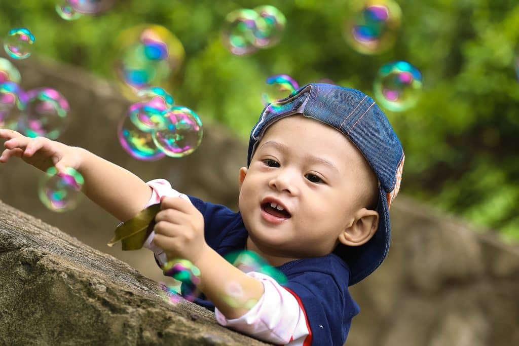 Asian boy in blue baseball cap, outside catching bubbles