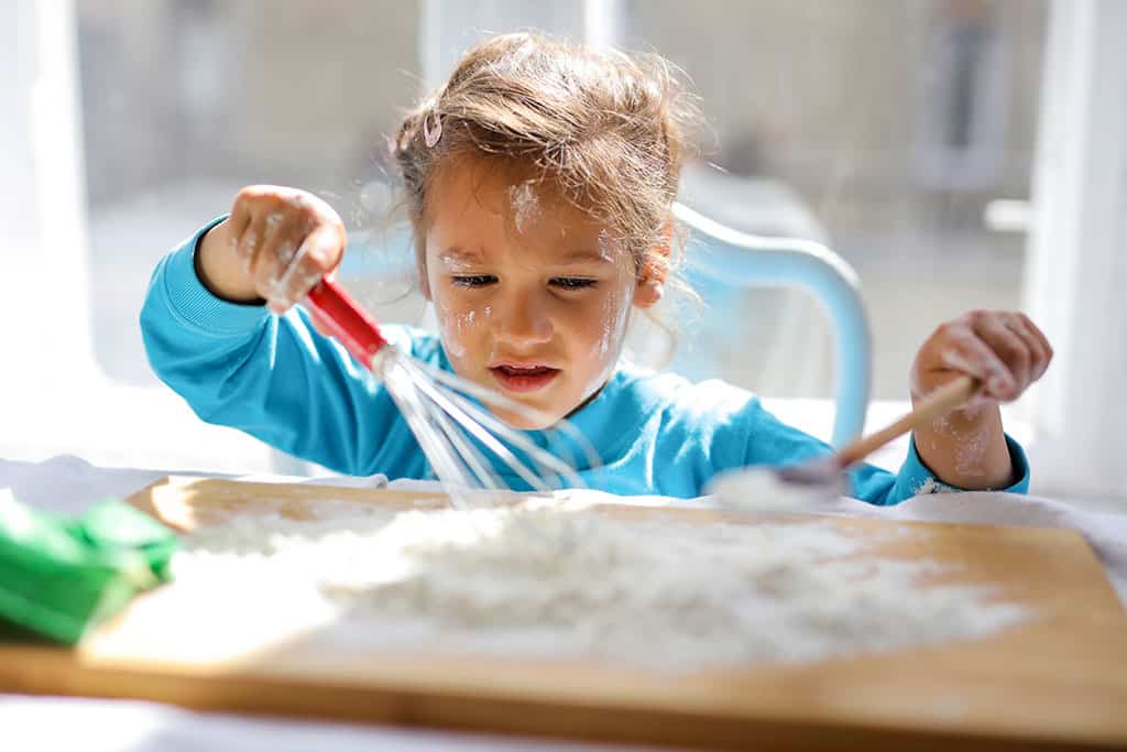 White child playing with flour and a whisk on a table