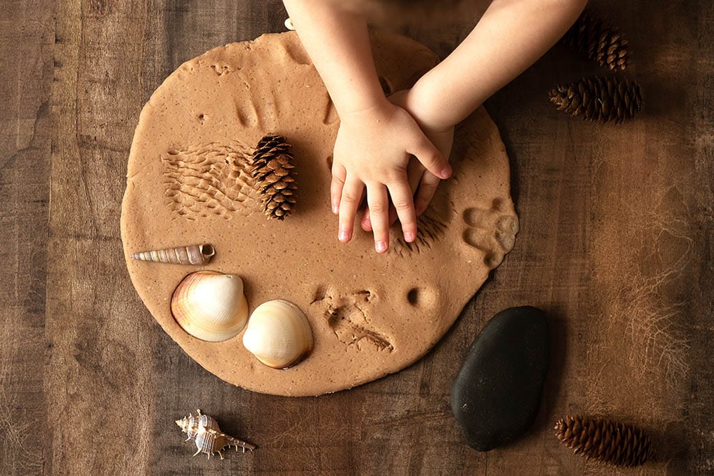 White hands playing with play dough with natural materials