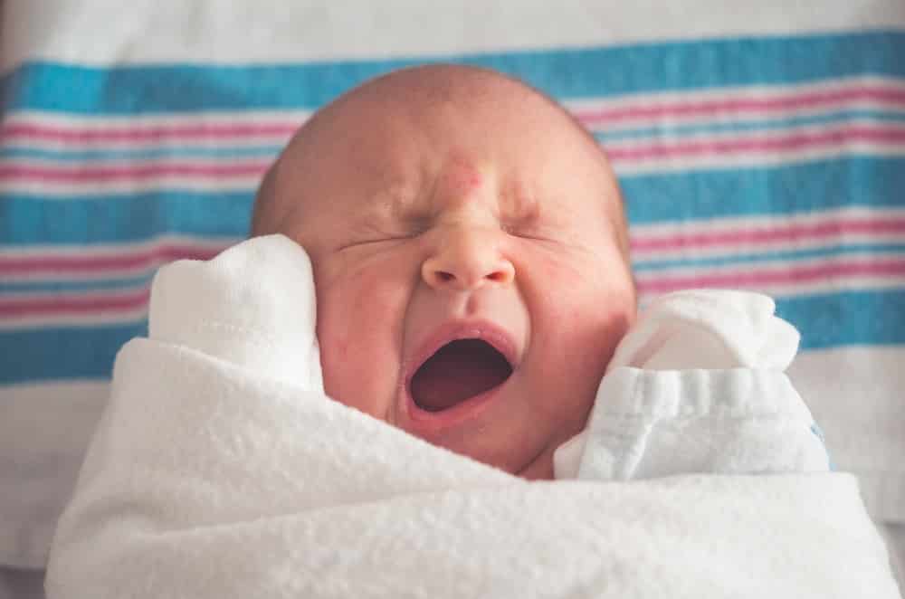 white appearing newborn baby yawning on a striped blanket