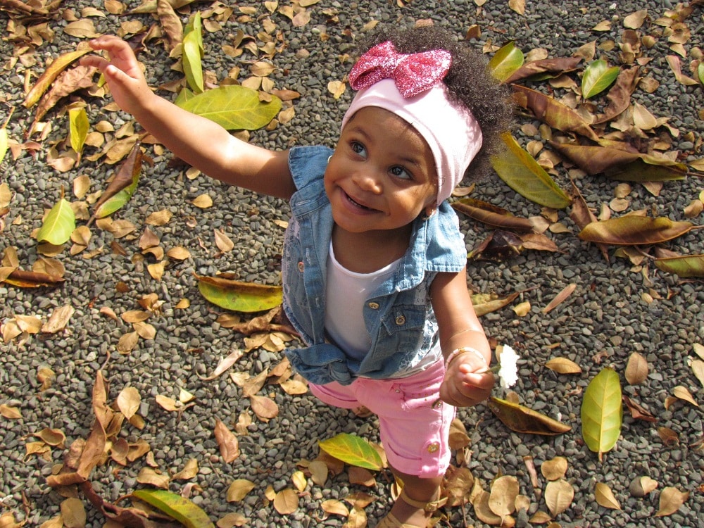 Dual heritage appearing child with pink bow in hair playing in Autumn leaves