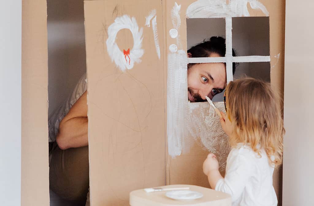 White appearing child painting a cardboard bow with father peeping through