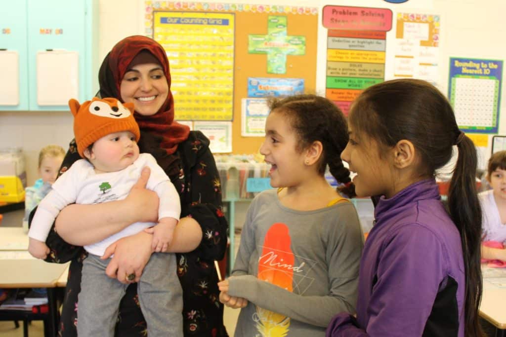 Mother in headscarf smiling with her baby and two school female school pupils