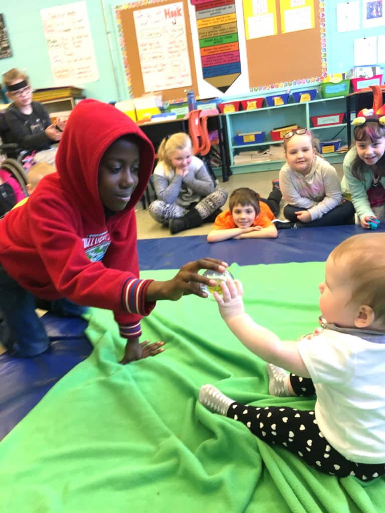 Young boy in red hoodie passing a ball to a baby