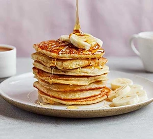 Stack of pancakes with banana and honey on a white plate