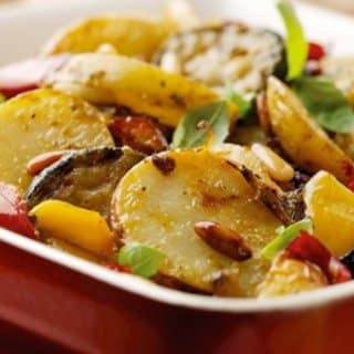 colour image of a potato and Mediterranean traybake in a white bowl on a red table 