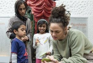 White appearing museum worker and three Asian children talking about an exhibit