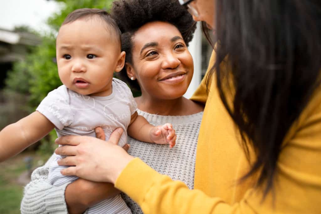 Black female couple talking and smiling holding a baby 