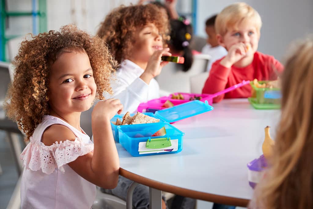 Group of young children eating lunch from lunchboxes