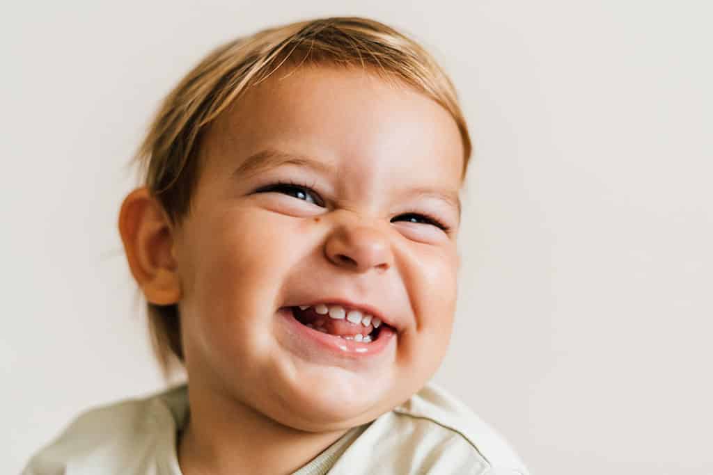 white toddler boy smiling at camera with teeth showing on white background