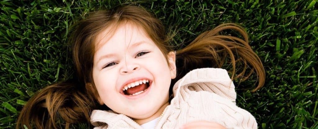 white, pre-school girls smiling with moth open laying on grass