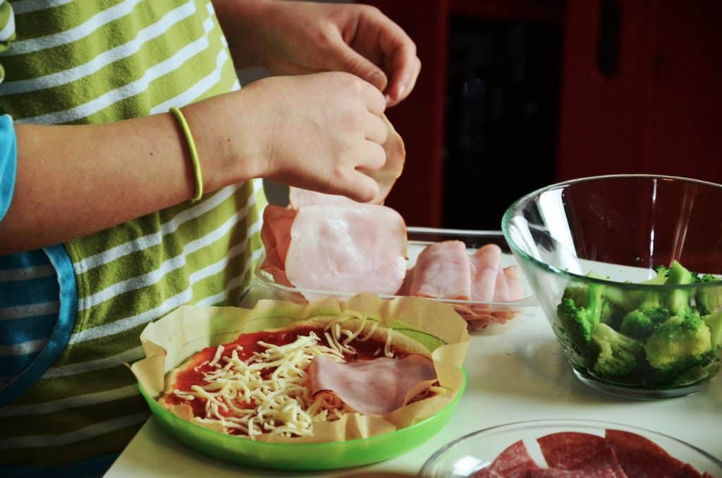 White adult and child preparing homemade pizza close up of hands and ingredients