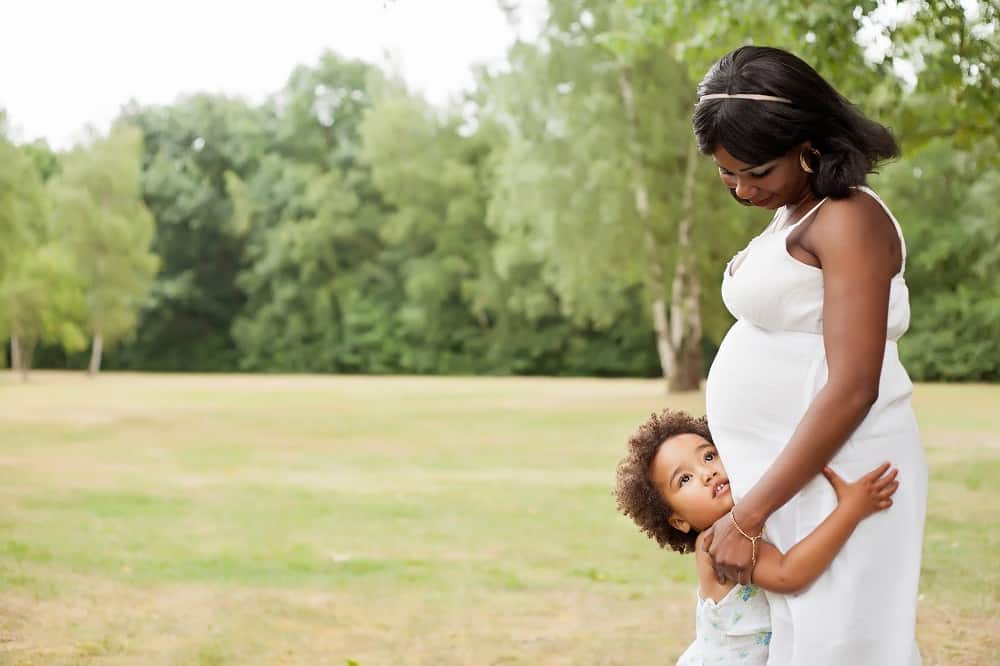 Black pregnant woman with black appearing toddler cuddling in park