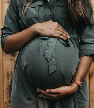 Black mum in a grey dress cradling her baby bump