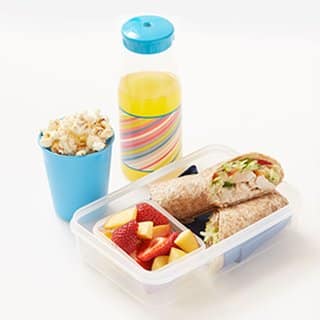 Photo of a lunch box containing a Spicy Chicken and salad wrap, a blue cup filled with popcorn and a small drink bottle filled with squash