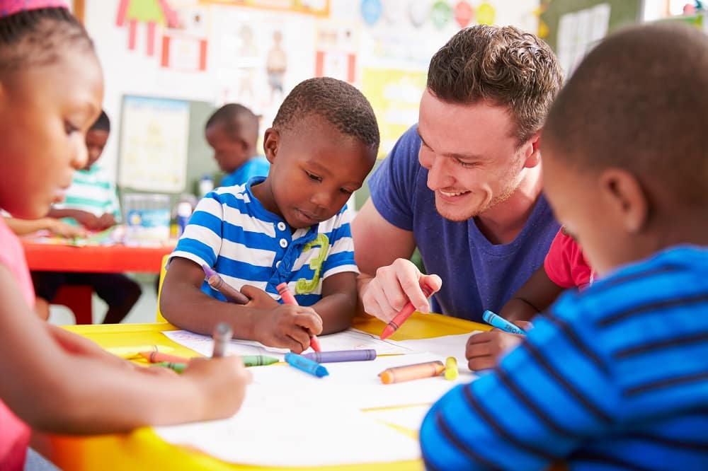 White teacher helping a class of black preschool kids drawing