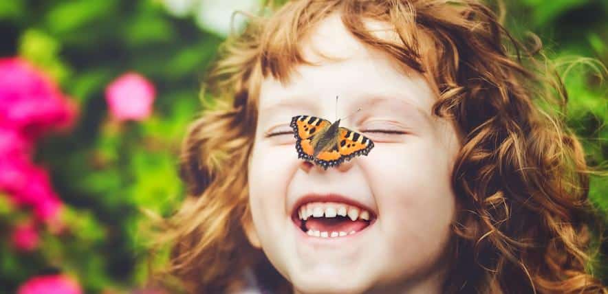 white red haired toddler laughing whilst a butterfly lands on her nose