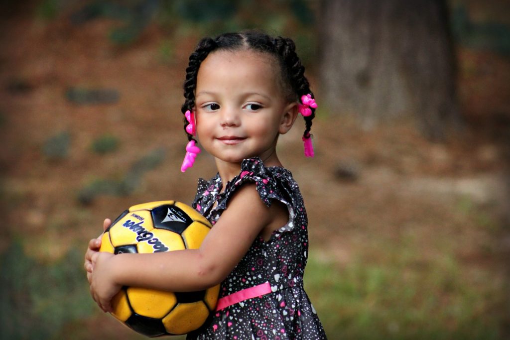 Mixed race appearing girl with plaits holding a black and yellow football outside