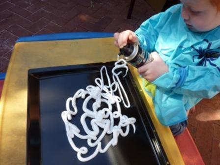White child squirting shaving foam onto a black tray