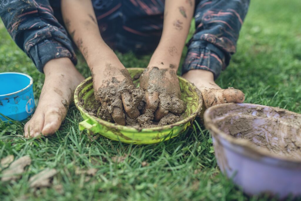 White child's hands squishing mud in a green bowl