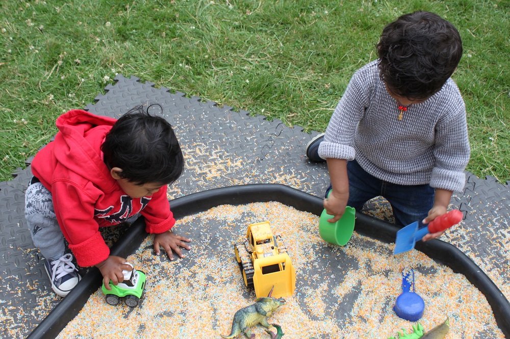 Two young Asian appearing boys playing with diggers and tools in a sand tray