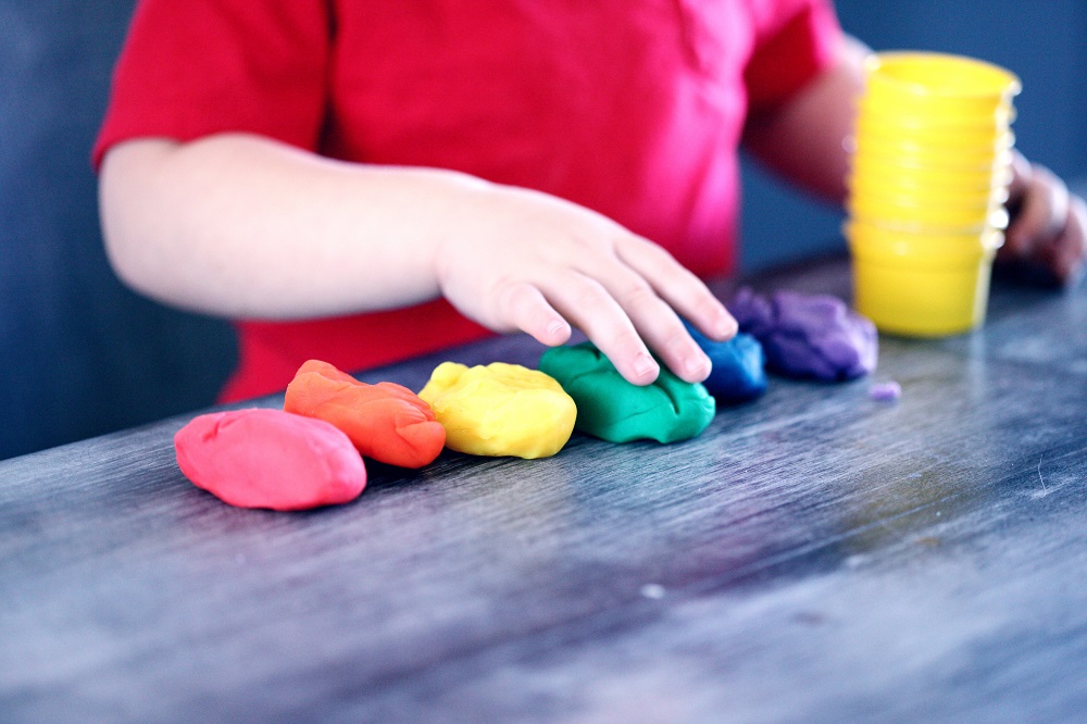 Young child's hand playing with bright coloured paly-doh