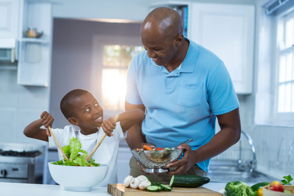 Black father and son smiling and preparing healthy food in kitchen