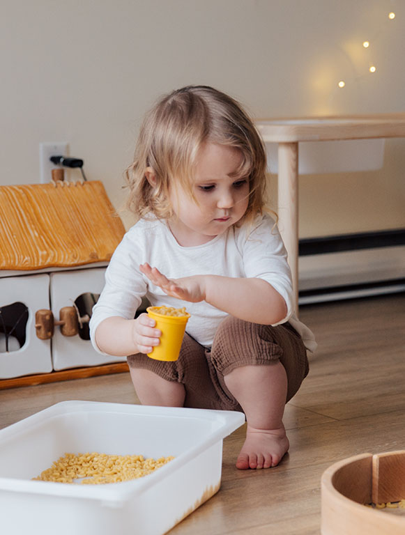 White toddler girl playing with pasta in a bowl