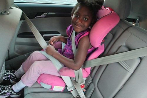 Young girl in wearing pink strapped into a pink car seat in the car