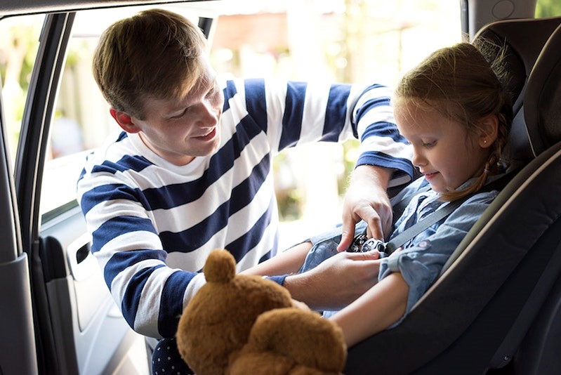 Dad strapping young girls in blue dress into car seat in the car