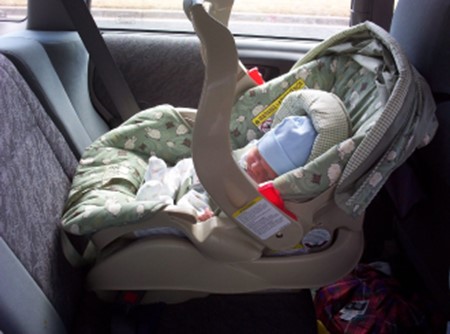 tiny baby in blue hat strapped into car seat in the car