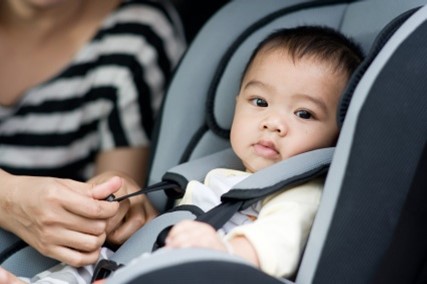 baby in white outfit being strapped into car seat in the car