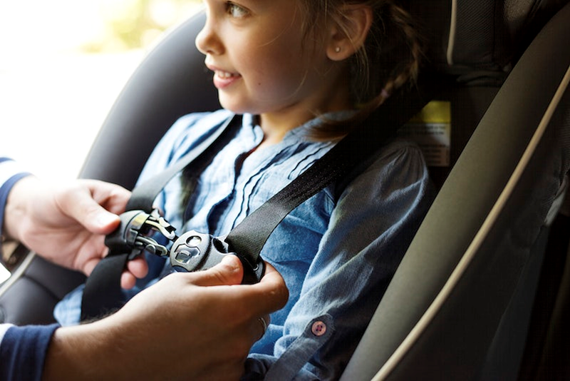 Young boy in blue shirt being strapped into car seat in the car