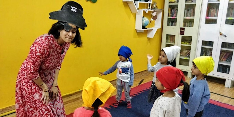 Female Asian teacher and children dressed up with pirate hats and pirate headscarves having fun in a yellow room. 
