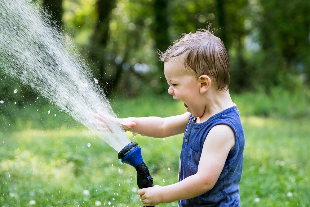 White toddler boy in blue vest playing with a hosepipe