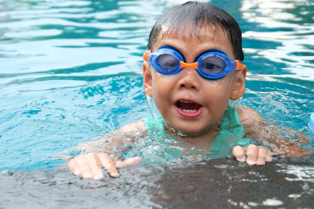 Asian toddler wearing blue goggles in a swimming pool