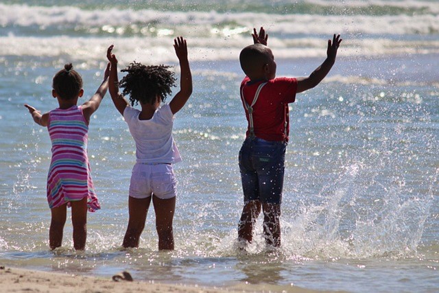 three black children in Summer clothes in the sea at the seaside 