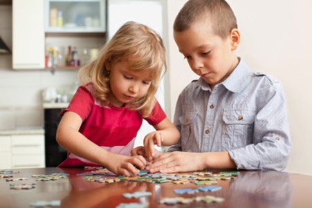two white young children completing a jigsaw puzzle on a table. 
